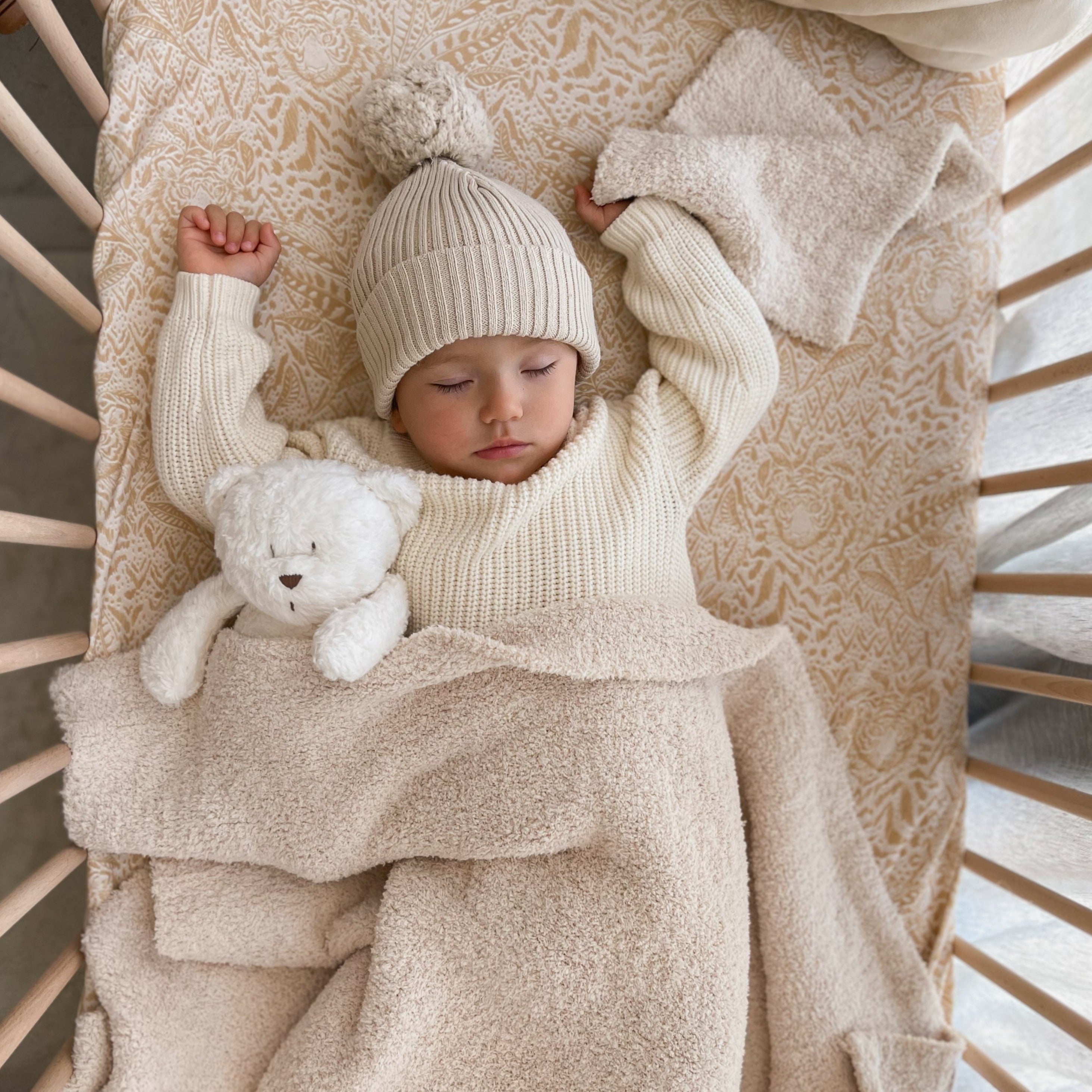 Baby in a cot with cozy neutral blanket